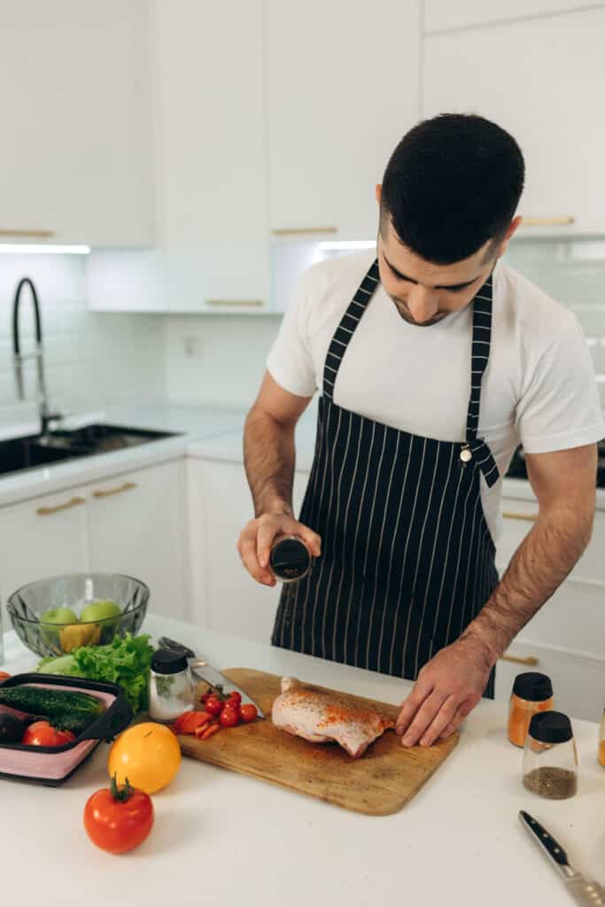 About Me 2 Aaron seasoning meat on a wooden board in a clean, modern kitchen