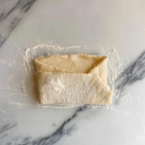 Folded rectangle of gluten free croissant dough on floured surface