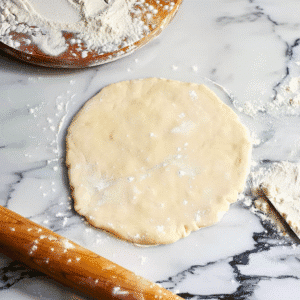 Pie crust dough rolled out on a marble surface with rolling pin