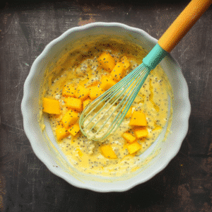 Mango chunks and chia seeds being mixed into pudding base